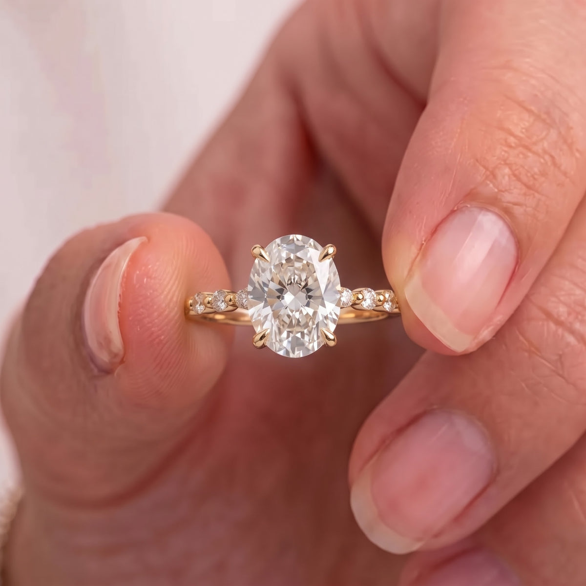 Oval brilliant lab-grown diamond ring in yellow gold held on hand showcasing elongated VVS/VS stone sparkle.