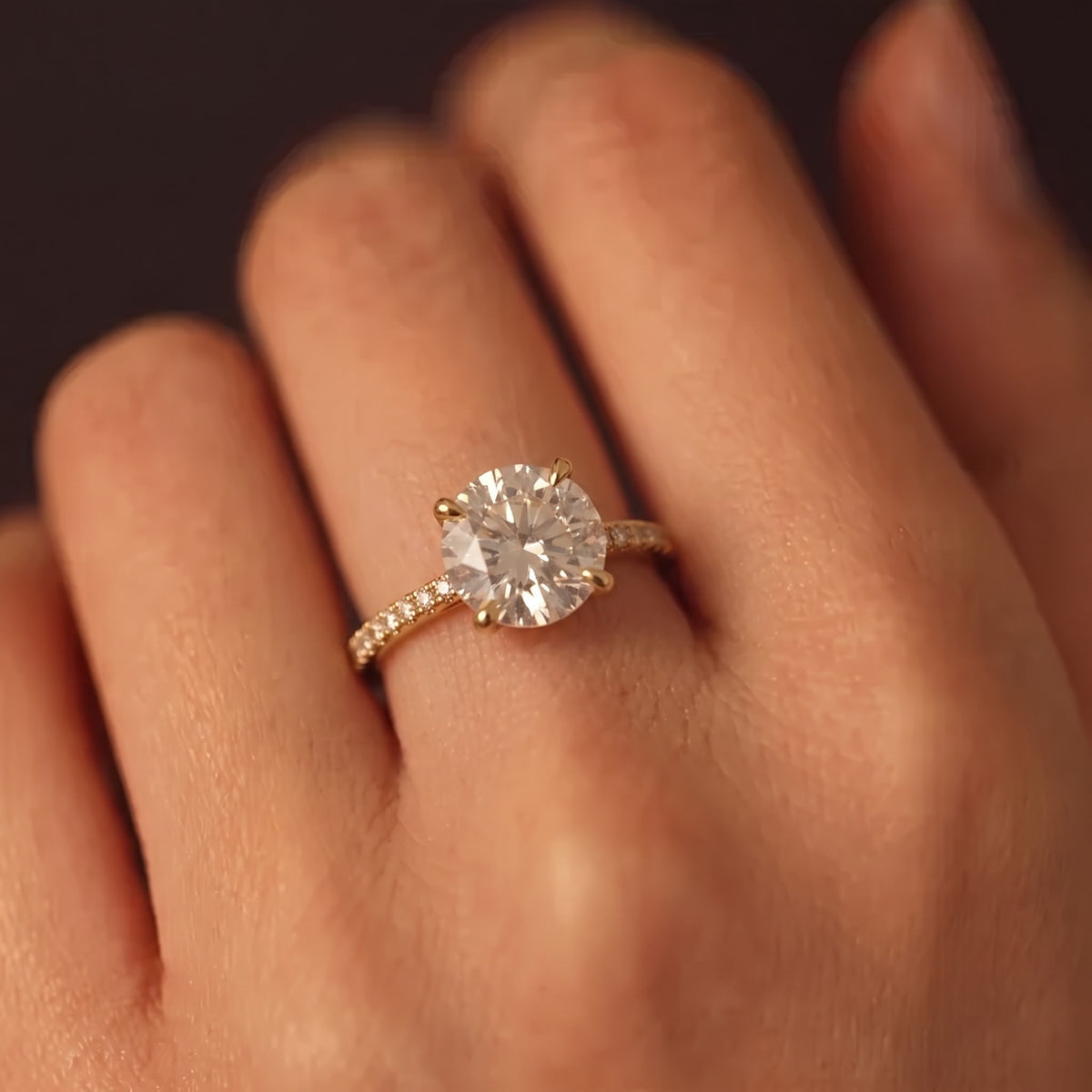 Round lab-grown diamond twisted pavé solitaire engagement ring in yellow gold worn on a model's hand