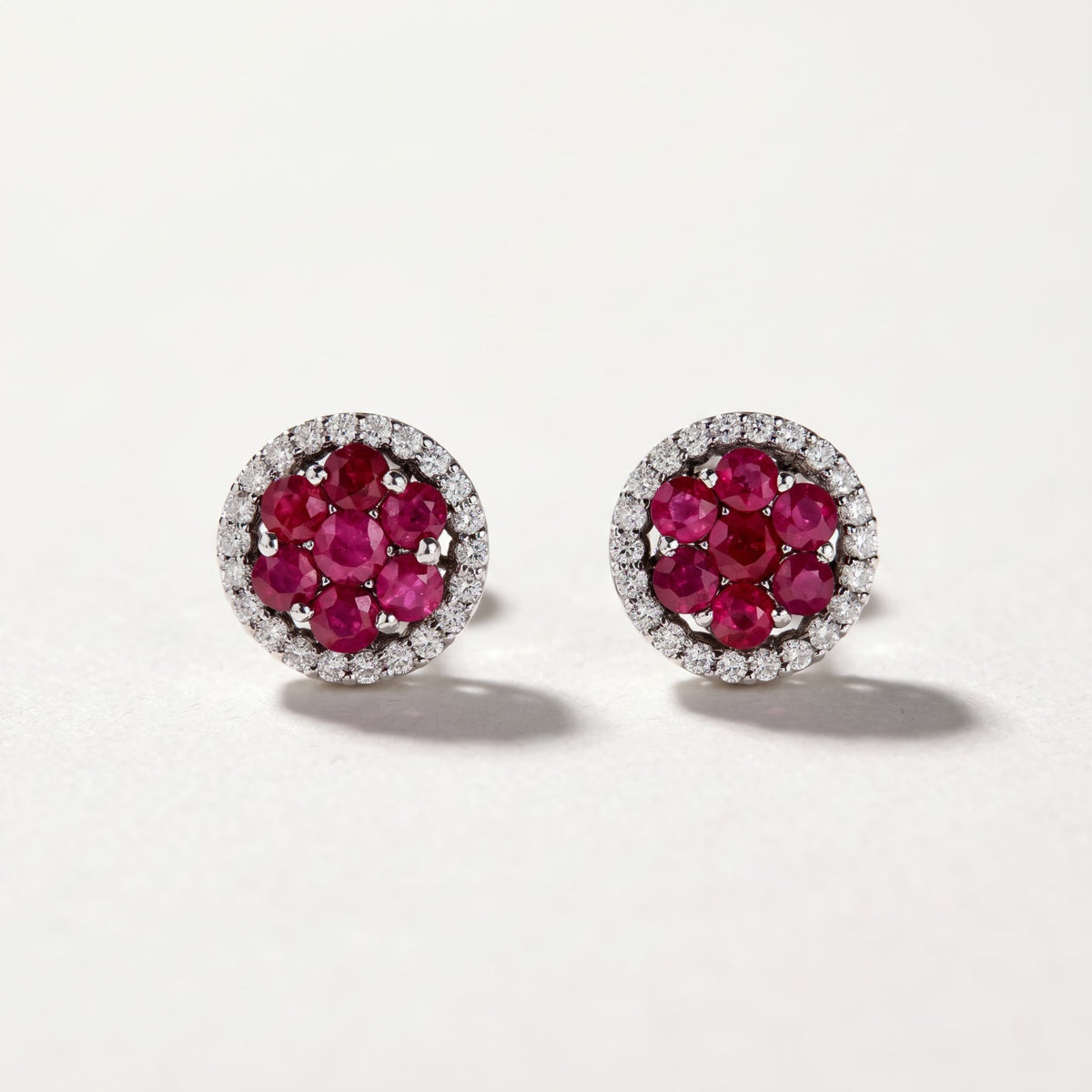 Pair of 18K white gold ruby and diamond stud earrings featuring round red rubies and diamond halos