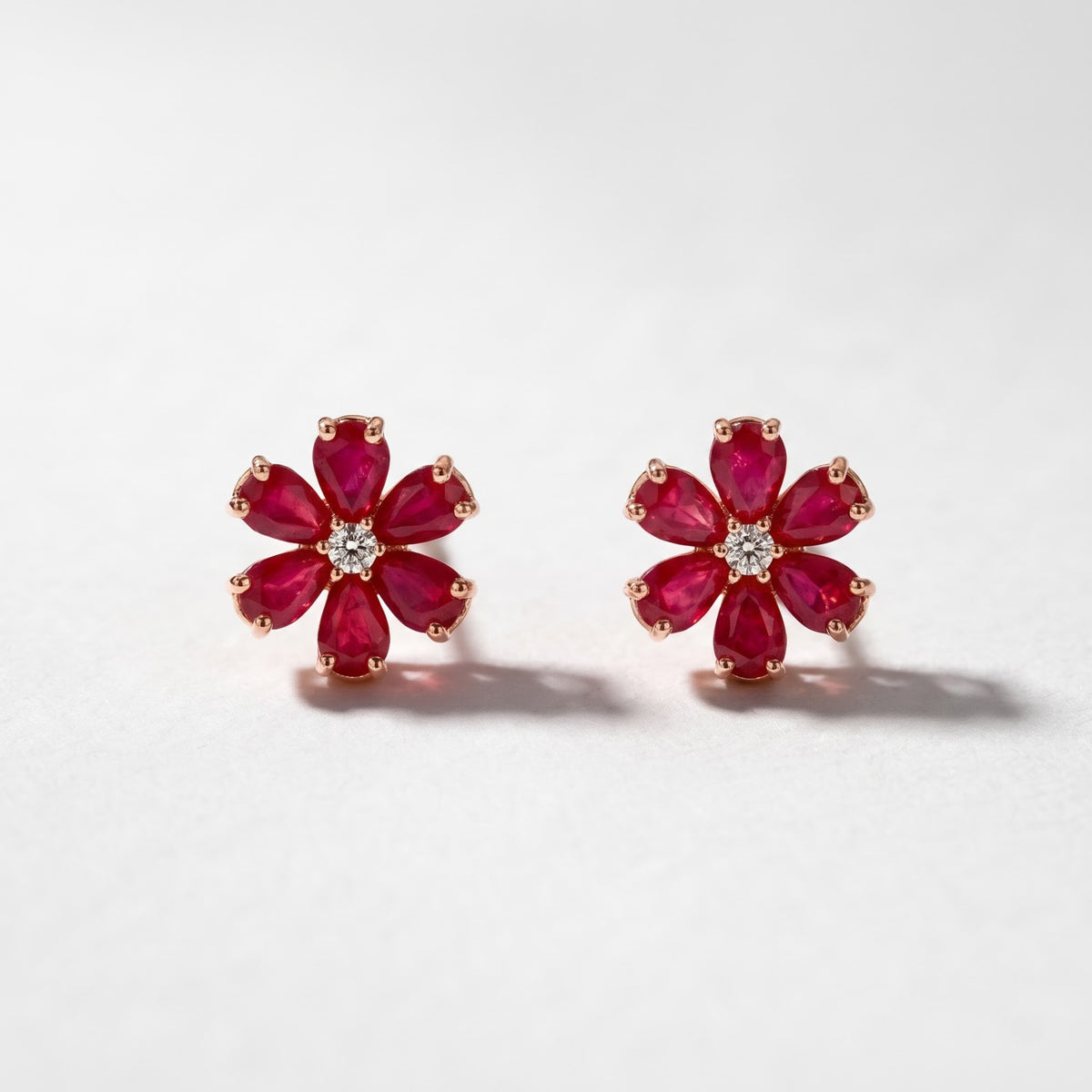 Pair of 14K rose gold ruby flower earrings featuring pear-shaped red rubies with round center diamond