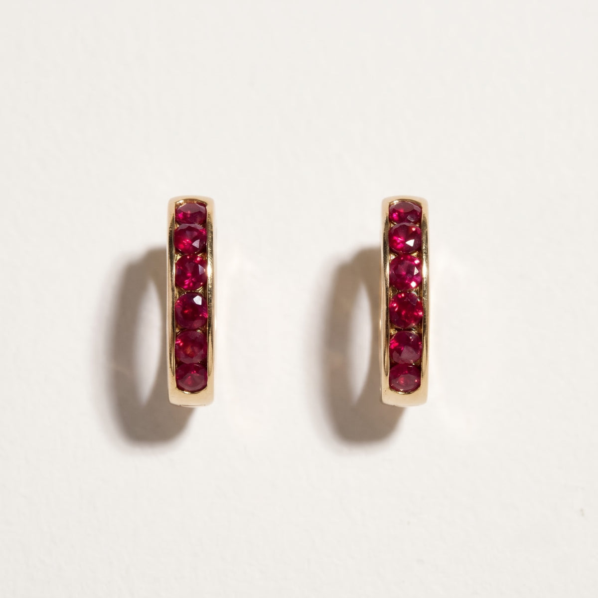 Pair of 14K yellow gold channel set ruby hoop earrings with round red rubies in 5/8 inch silhouette