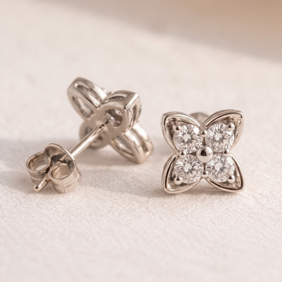 A pair of silver butterfly stud earrings with clear round-cut gemstones, shown on a textured off-white surface. One earring is shown from the front displaying the butterfly face, and the other is turned to show the post and butterfly back.