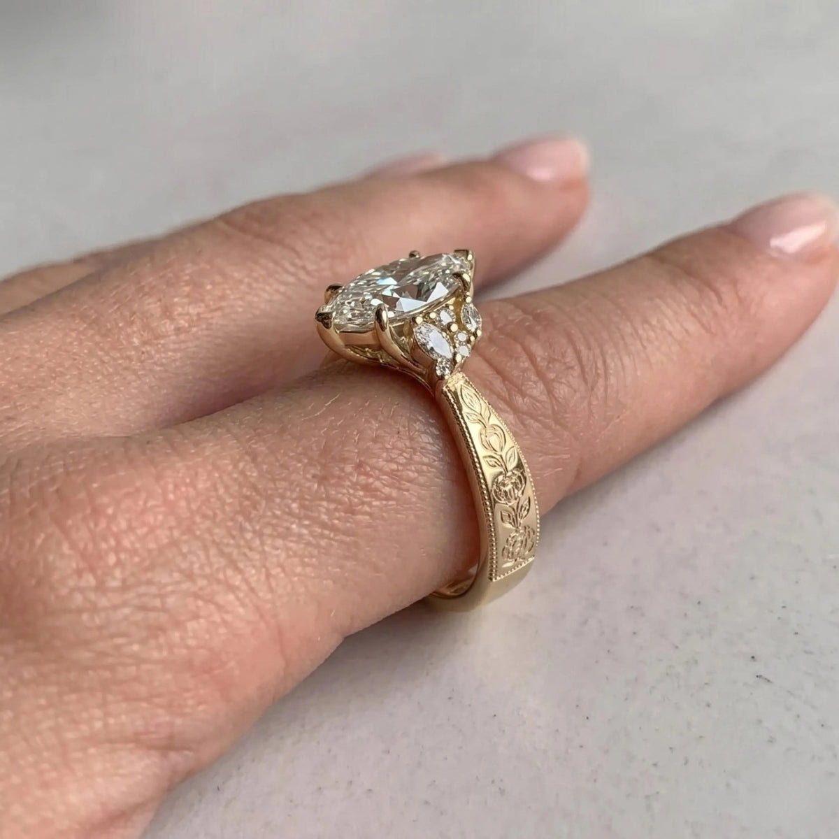 Yellow gold Art Deco engagement ring with a marquise center stone and engraved band, worn on a hand.