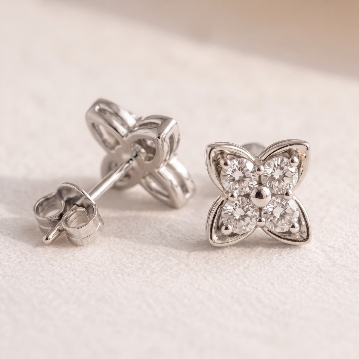 A pair of silver butterfly stud earrings with clear round-cut gemstones, shown on a textured off-white surface. One earring is shown from the front displaying the butterfly face, and the other is turned to show the post and butterfly back.