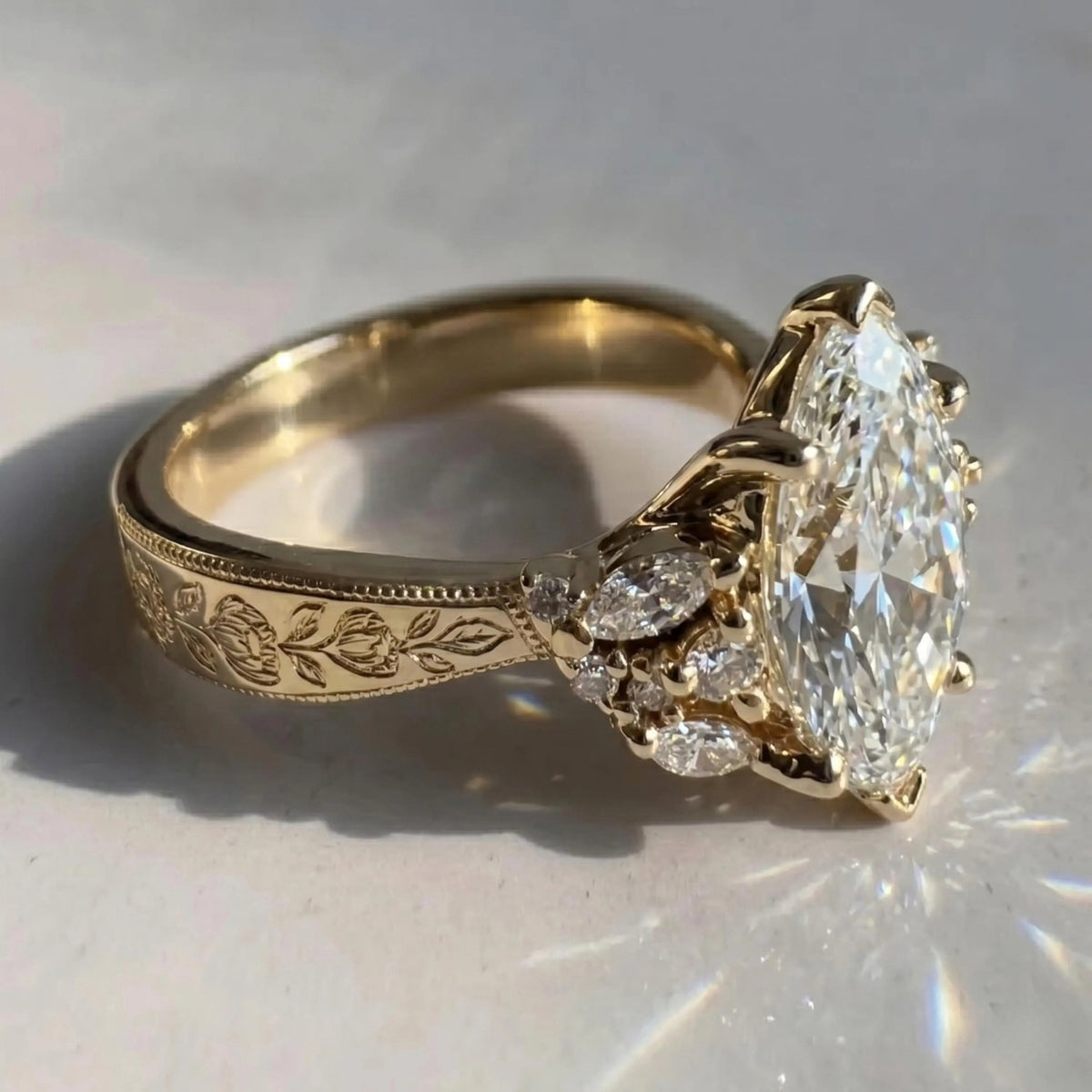 Close-up of a yellow gold Art Deco engagement ring with a marquise center stone, floral cluster accents, and an engraved band.