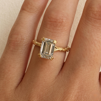 A close-up of a hand wearing a gold ring with a large emerald-cut clear gemstone.