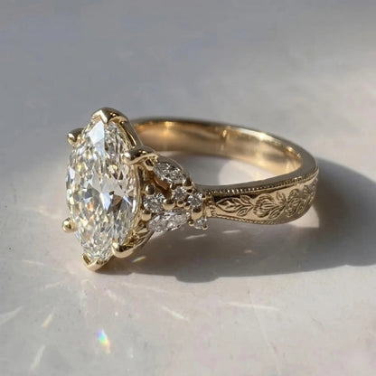 Close-up of a yellow gold Art Deco engagement ring with a marquise center stone, floral cluster accents, and an engraved band.