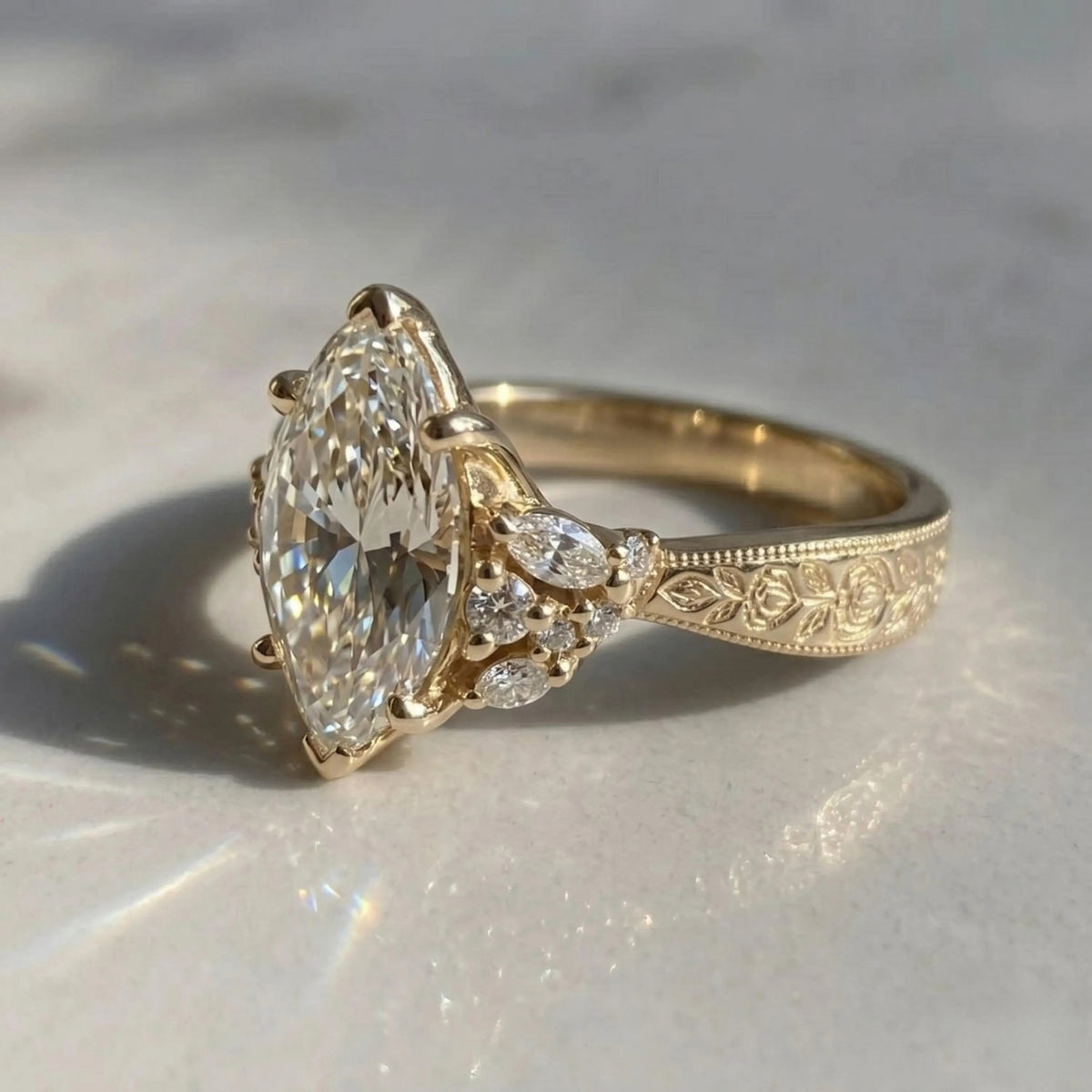 Close-up of a yellow gold Art Deco engagement ring with a marquise center stone, floral cluster accents, and an engraved band.