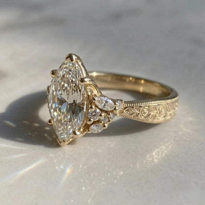 Close-up of a yellow gold Art Deco engagement ring with a marquise center stone, floral cluster accents, and an engraved band.