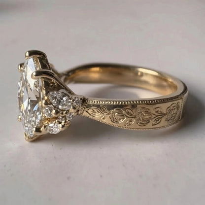 An antique-style yellow gold ring featuring a large marquise-cut diamond as the center stone, accented by small round diamonds on the shoulders and an engraved floral pattern on the band, set against a neutral light gray background.