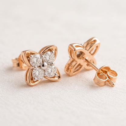 A pair of rose gold flower stud earrings with clear round-cut gemstones, shown on a textured off-white background. One earring is facing forward to show the front design, and the other is turned to show the back post and backing.